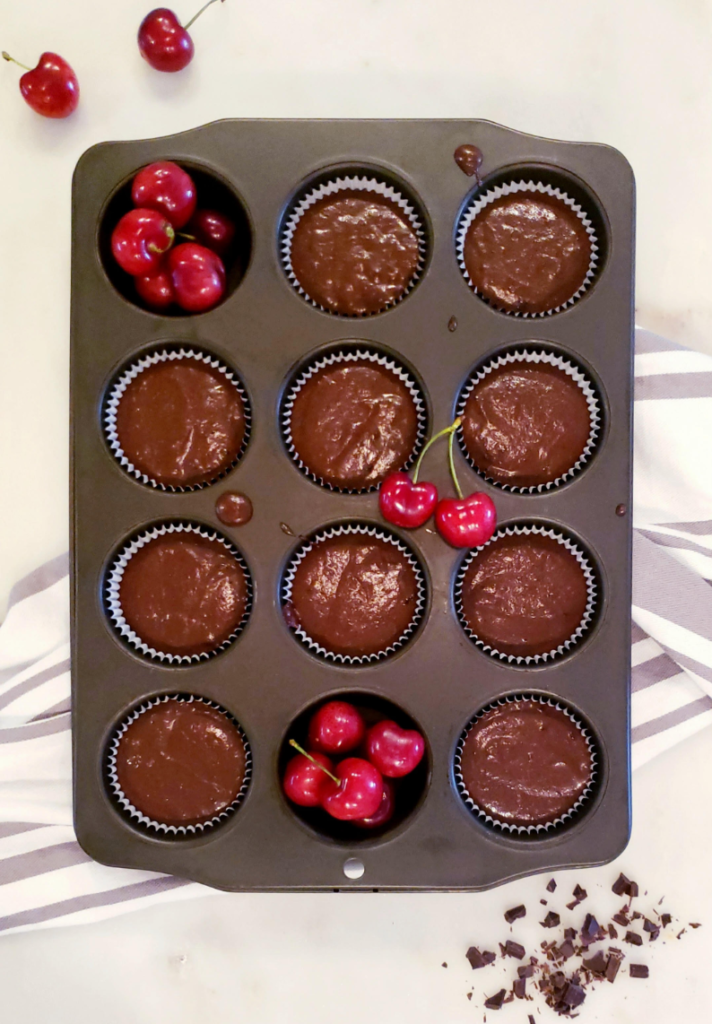 Functional image black forest cupcake batter in a cupcake pan with cupcake liners fresh Bing cherries and chopped chocolate