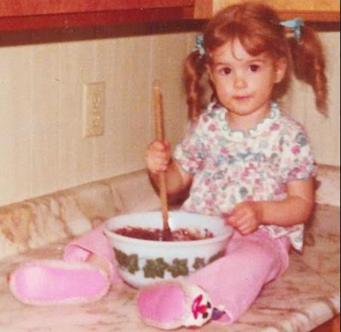 About me photo Whisking Wolf young Heather Wolf with a mixing bowl of brownie batter