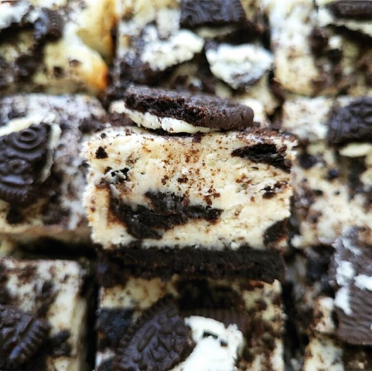 oreo cheesecake bars cut into squares. close up view of a cheesecake bar topped with broken oreo cookies.