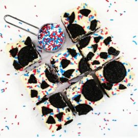 functional image oreo funfetti cheesecake bars top down view eight square slices with a measuring cup full of funfetti sprinkles where the ninth slice should be