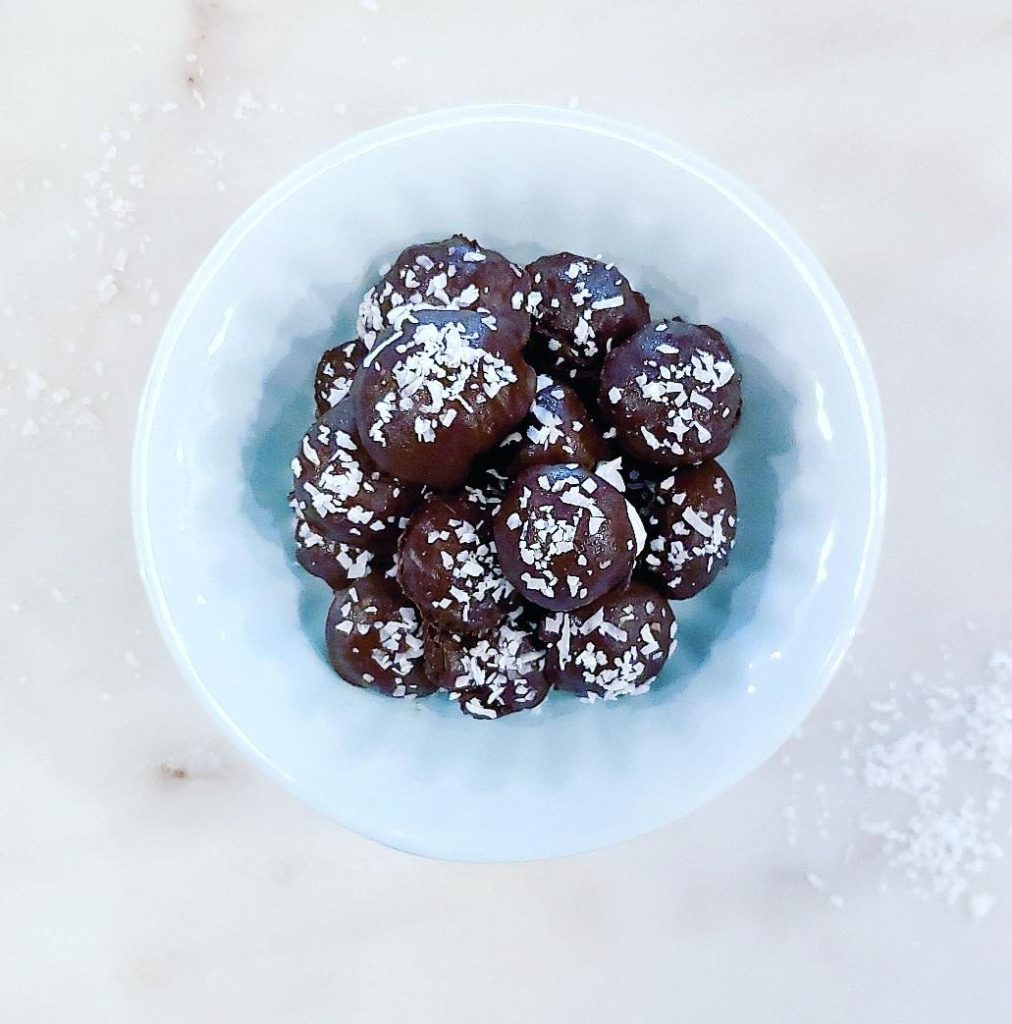functional image dark chocolate coconut rum truffles with flaked coconut piled on top in a baby blue bowl on a white marble surface