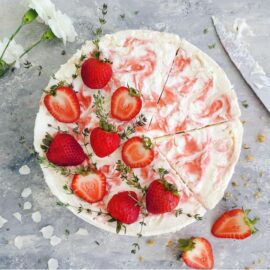no bake strawberry swirl cheesecake. top down photo of cheesecake garnished with fresh strawberries and thyme sprigs. three slices have been cut but not removed.