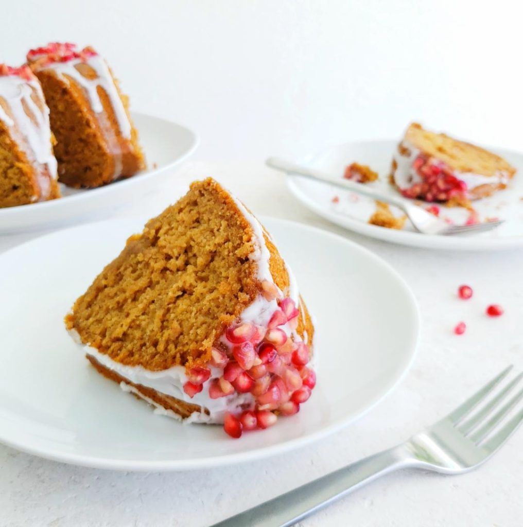 functional image bourbon honey bundt cake side view slices on white plates to showcake moist texture glaze and pomegranate seeds three plates and two forks on white background