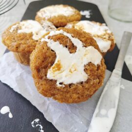 sweet potato muffins with marshmallow swirl on top. close up view of muffins on a black wooden cutting board splattered with marshmallow.