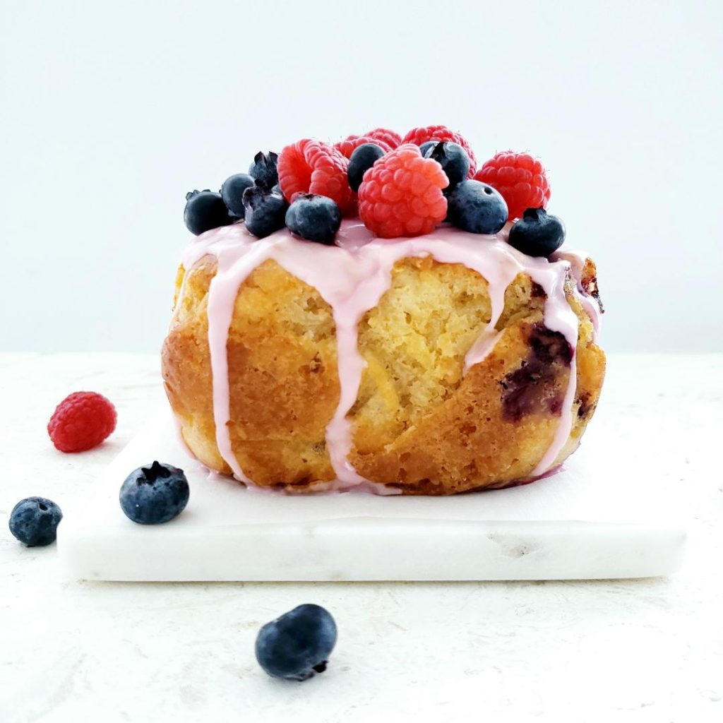 functional image side view of hard apple cider bread loaf is on a board of white marble pink raspberry glaze is dripping down the loaf and it is topped with fresh raspberries and blueberries beer bread recipe