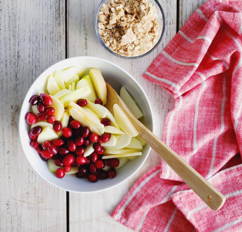 functional image cranberry apple crumble pie recipe ingredients in a white mixing bowl with a wooden spoon and a separate bowl of crumble top down photo