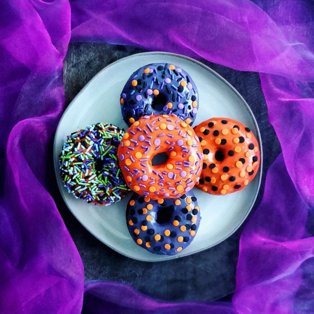 functional image halloween donuts  top down photo five frosted chocolate fall donuts each decorated differently for halloween on a gray plate with a purple tulle background