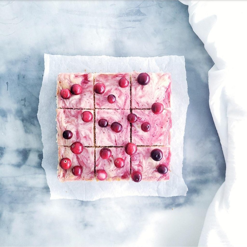 functional image cranberry cheesecake bars with graham cracker crust cut into 9 squares with fresh cranberries top down photo