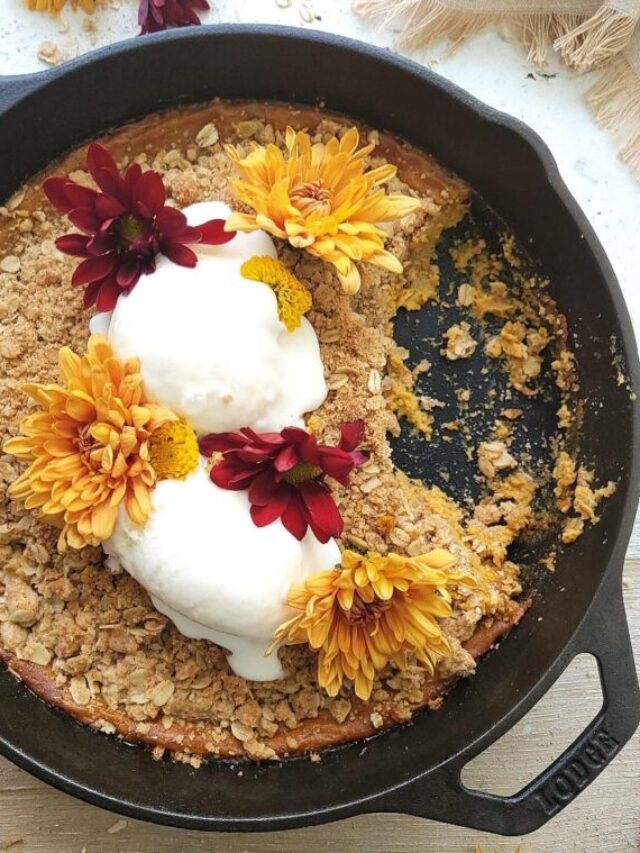 pumpkin crisp baked in a cast iron skillet. top down view of crisp garnished with scoops of vanilla ice cream and fall flowers. a section of the crisp has been scooped away and a few crumbs remain.