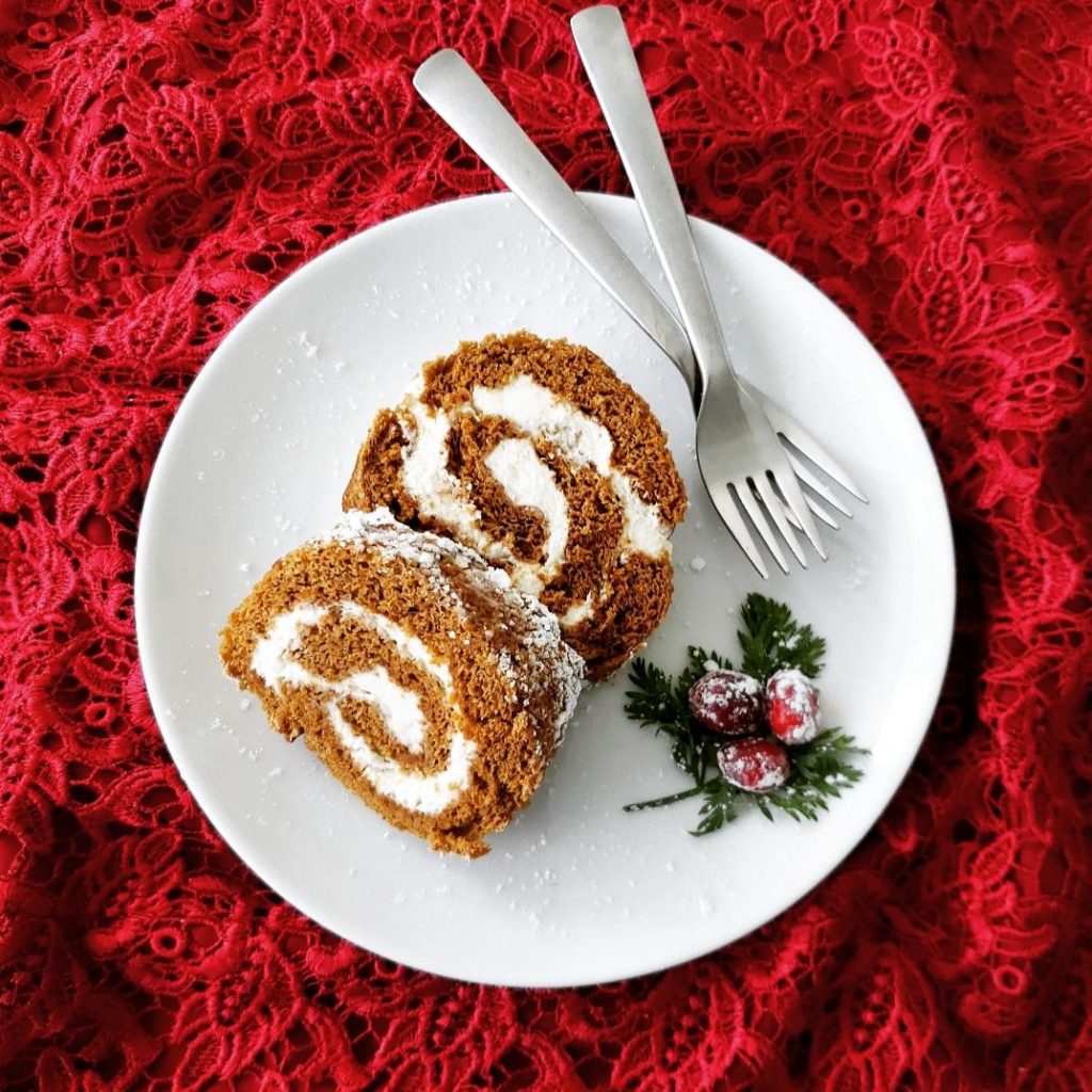 functional image gingerbread cake roll recipe with two slices on one plate with forks and sugared cranberries