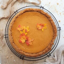 graham cracker crust pumpkin pie. top down view of uncut pie. pie is styled with tiny fall leaves and sits on a round black wire baking rack.
