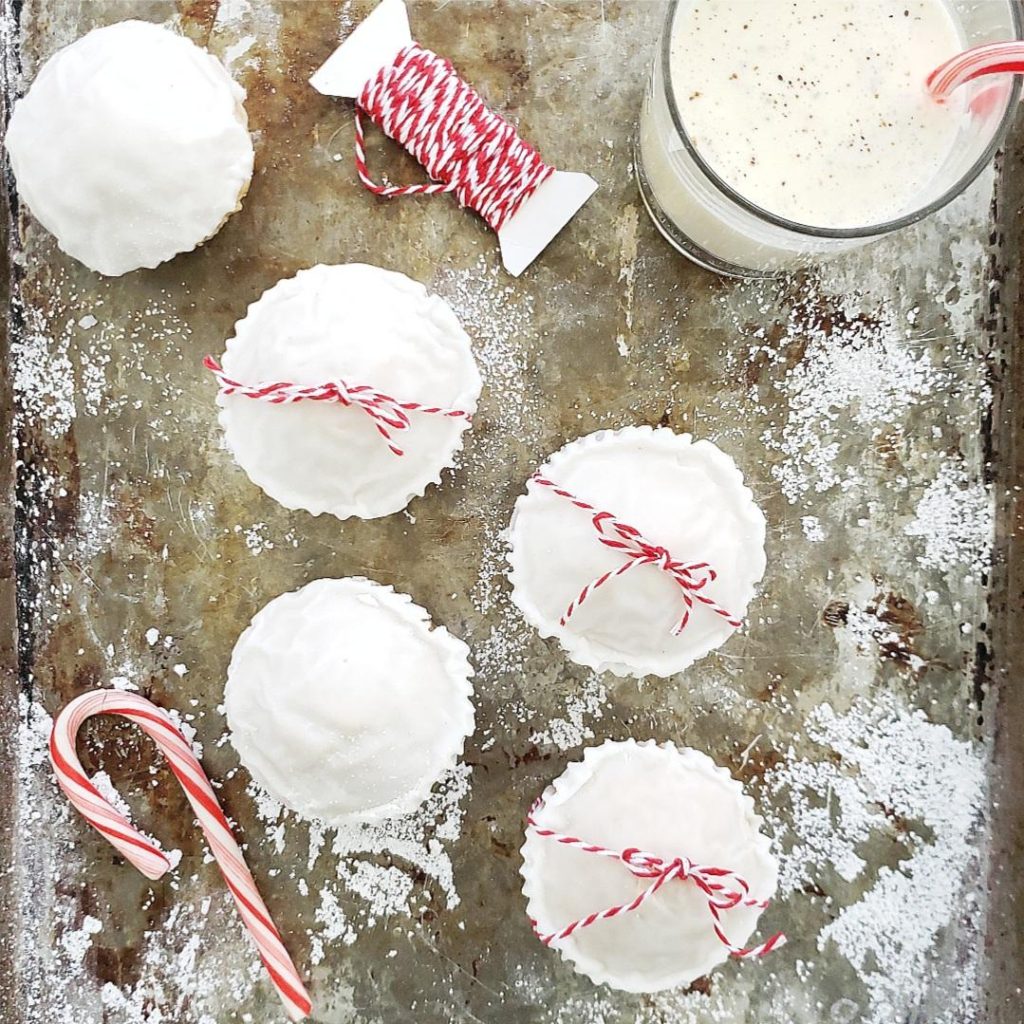 eggnog muffins recipe with eggnog glaze on a cookie sheet with a glass of eggnog and a candy cane