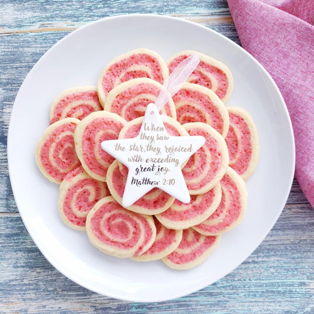 functional image peppermint pinwheel cookies with crushed candy canes piled on a white plate with a white star christmas ornament