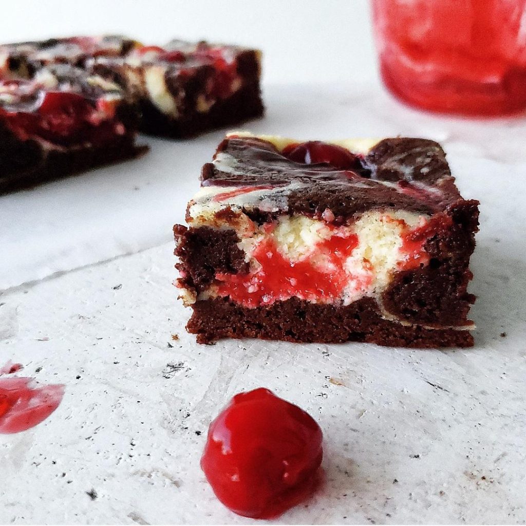small batch cherry cheesecake brownies one square cut front and center with a single cherry