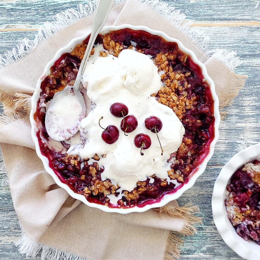 functional image cherry crisp with fresh cherries in pie plate with a spoon and a serving bowl