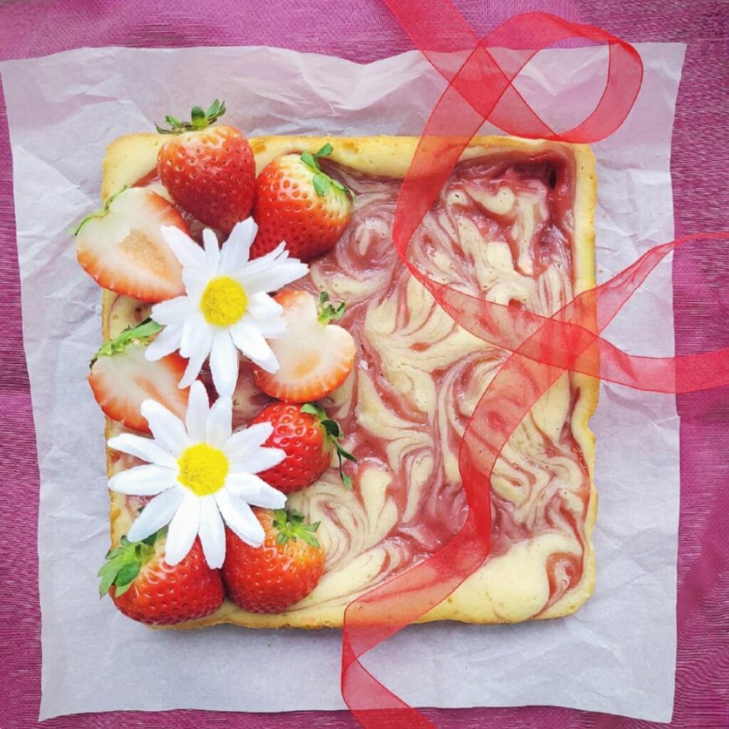 strawberry blondies. top down view of uncut strawberry swirl blondies topped with fresh strawberries and white daisies