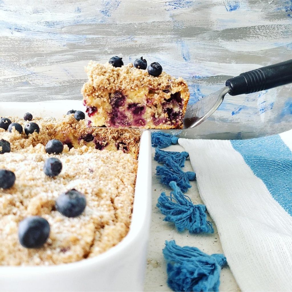 blueberry coffee cake with sour cream cut slice on spatula with crumb topping and fresh blueberries 