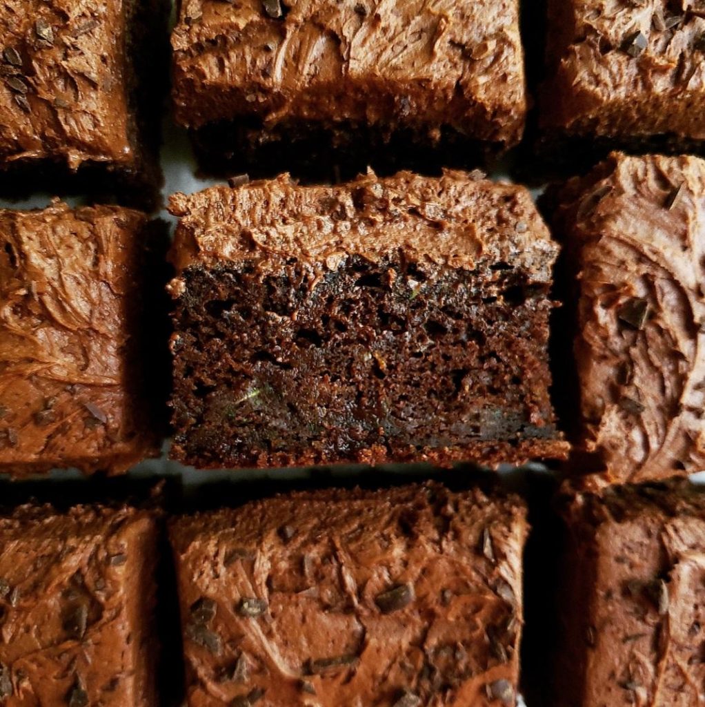 chocolate zucchini cake. close up view of chocolate sheet cake cut into squares and topped with chocolate frosting. one slice is turned on its side so you can see the moist inner crumbs