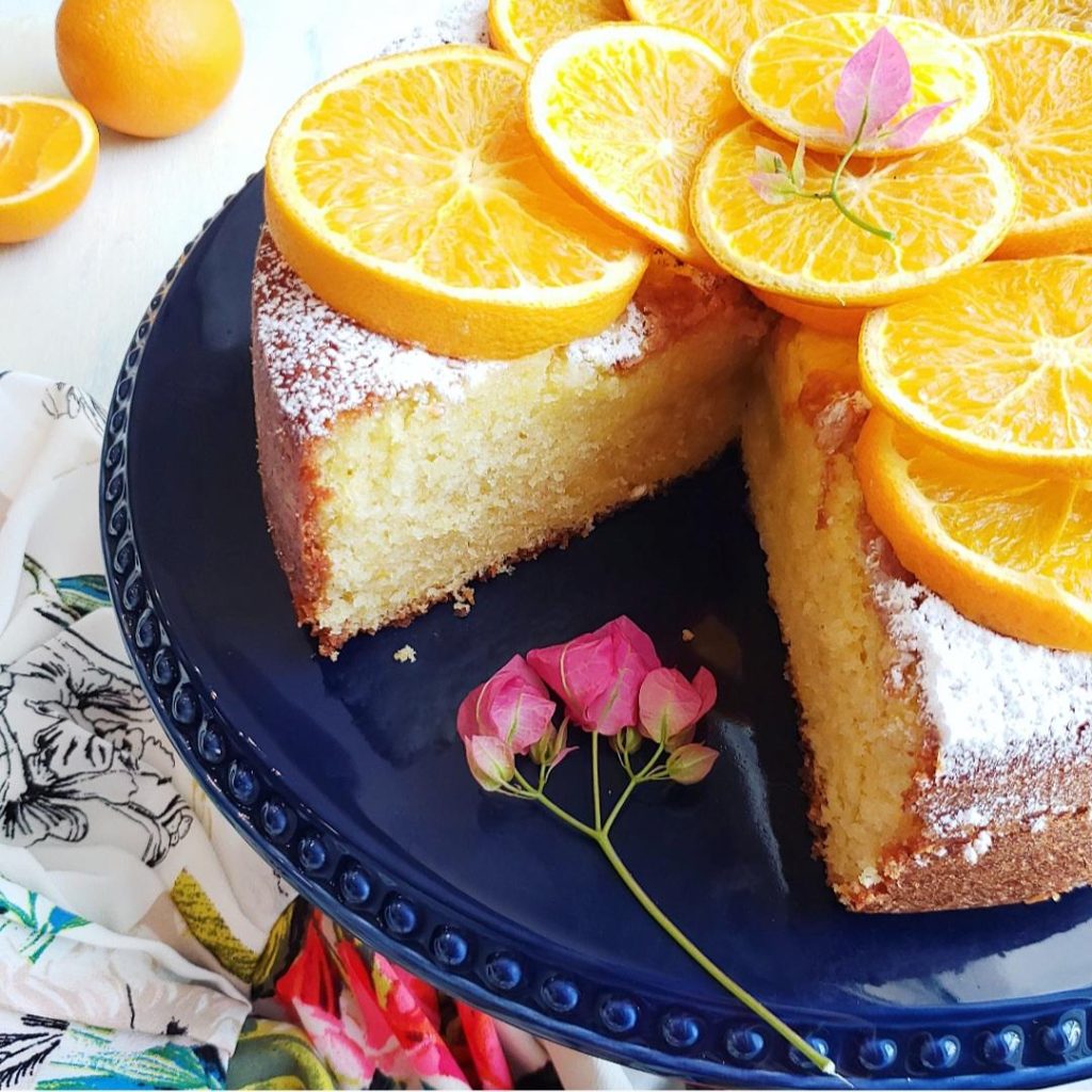 functional image olive oil orange cake cut on a cobalt blue cake stand garnished with fresh orange slices