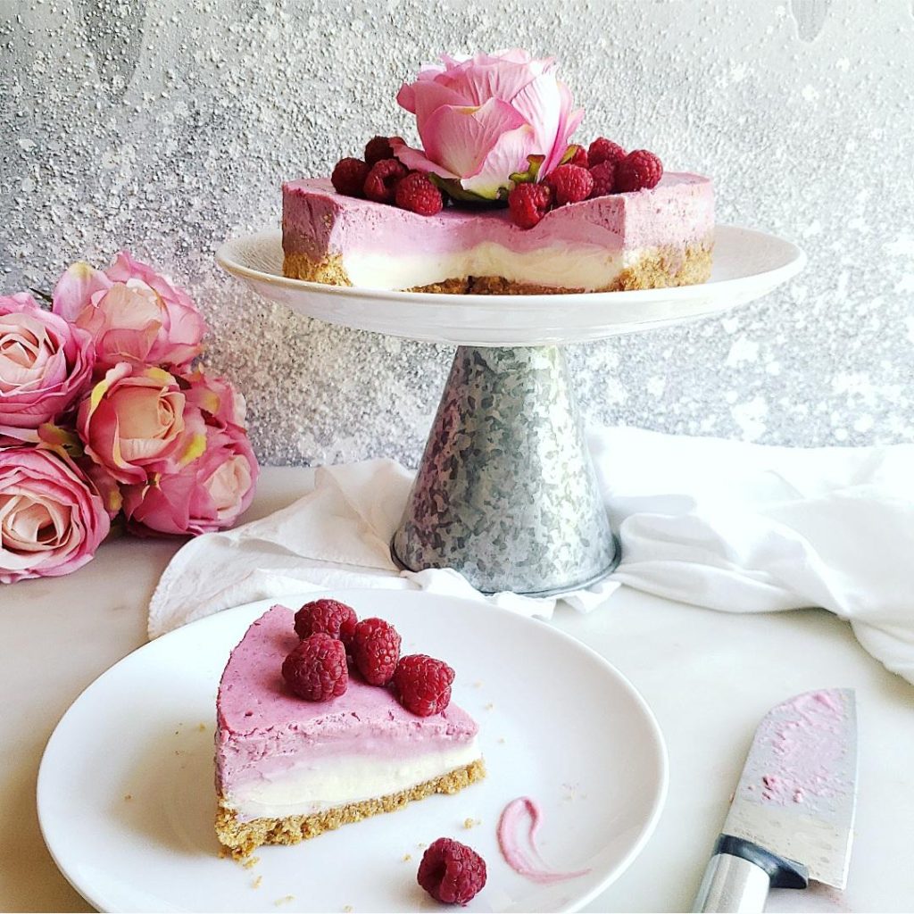 functional image raspberry cheesecake on a cake stand in the background one slice cut on a plate with fresh raspberries 