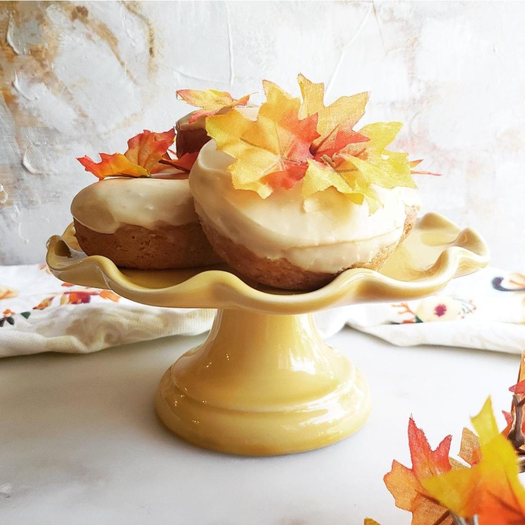 functional image maple donuts stacked on a pretty yellow cake stand with maple leaves and maple glaze