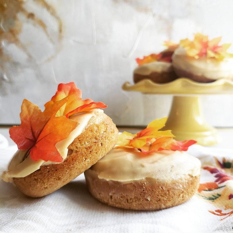functional image baked maple donuts with maple glaze and colorful maple leaves two in front and more stacked on a yellow cake stand in the background