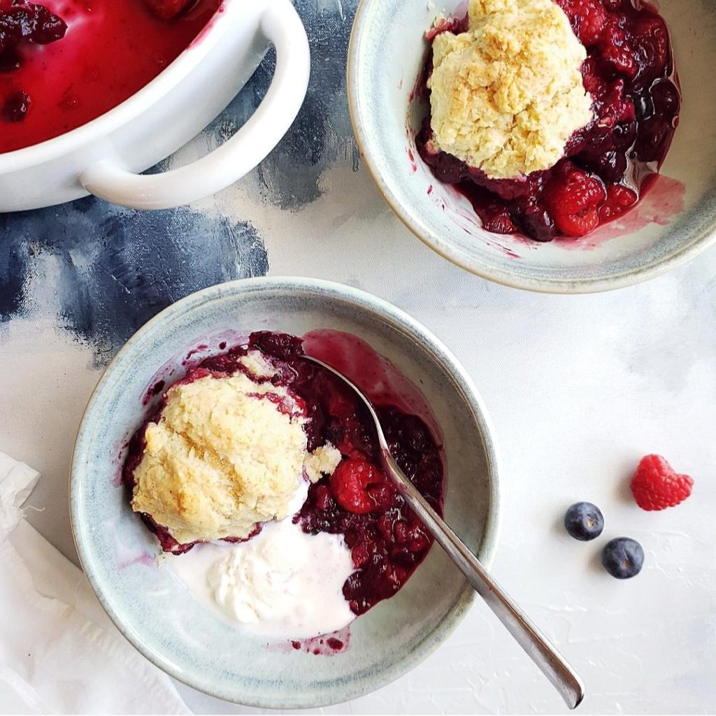 mixed berry cobbler top down photo of two pale blue bowls with biscuits spoons and baked fruit