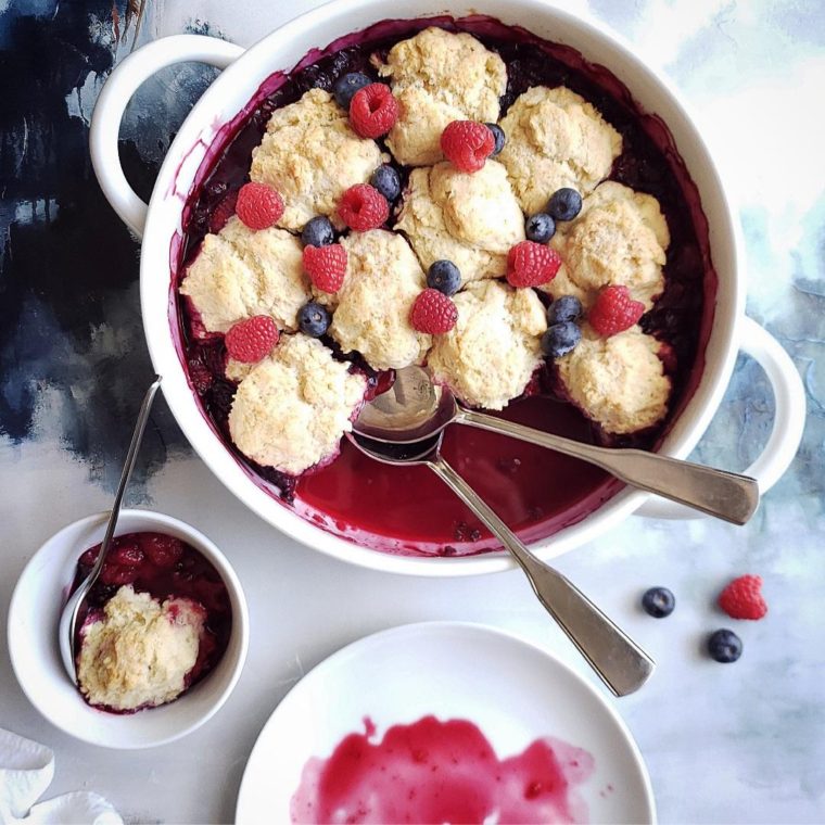 functional image mixed berry cobbler in white baking dish with fresh fruit and serving spoons