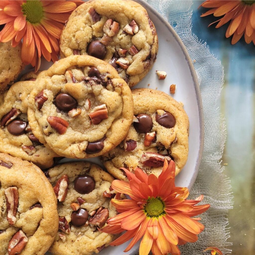 chocolate chip pecan cookies piled on a gray plate and garnished with fall flowers