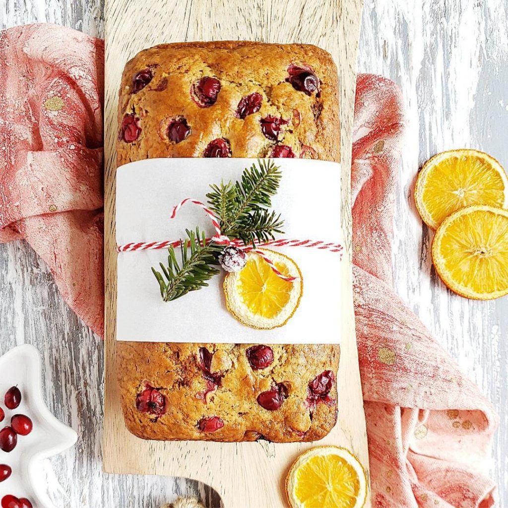 functional image cranberry orange bread top down unsliced wrapped for gift giving with a sprig of christmas tree and sugared cranberries and dehydrated orange slices