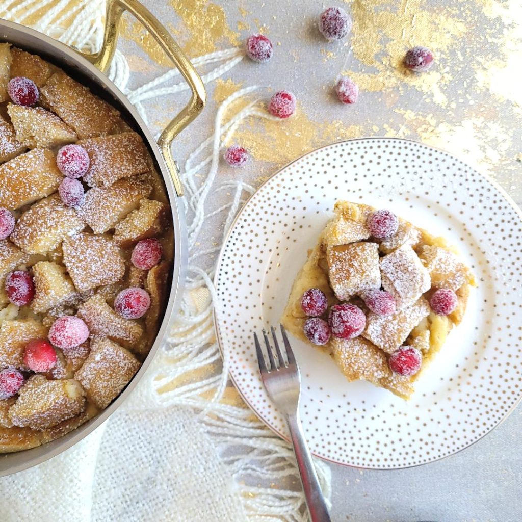 functional image eggnog bread pudding slice of dessert on gold polka dot plate on right hand side with sugared cranberries and powdered sugar