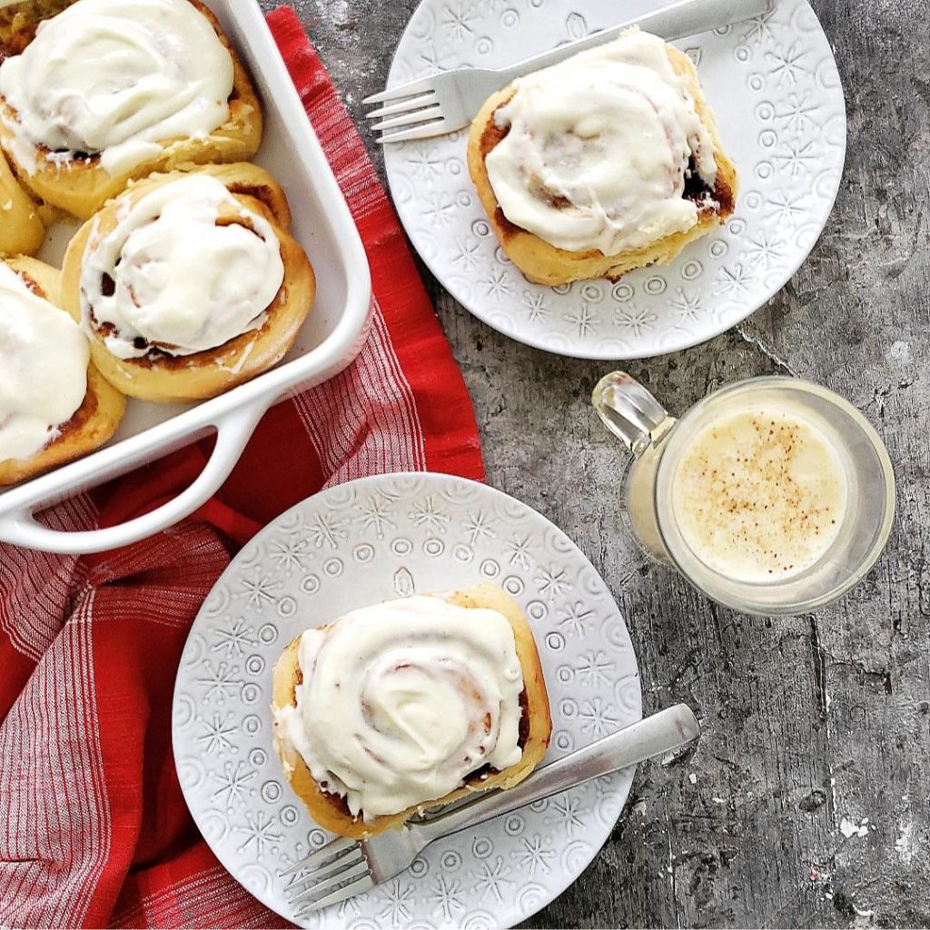 functional image eggnog cinnamon rolls recipe top down cinnamon rolls in the baking pan and one on a plate all are topped with icing