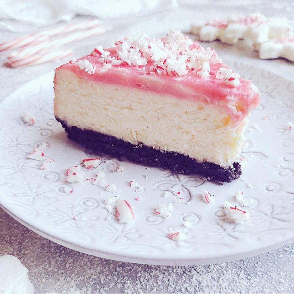 functional image peppermint cheesecake one slice on a plate topped with crushed candy canes side view so you can see layers oreo crust and white chocolate ganache dyed pink 