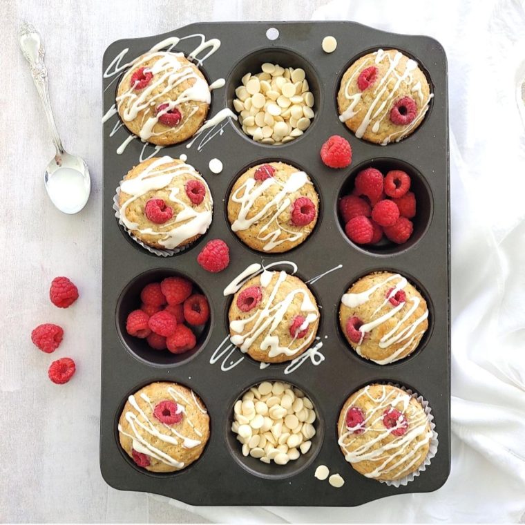 functional image raspberry muffins in a muffin pan top down with fresh raspberries drizzled with melted white chocolate chips