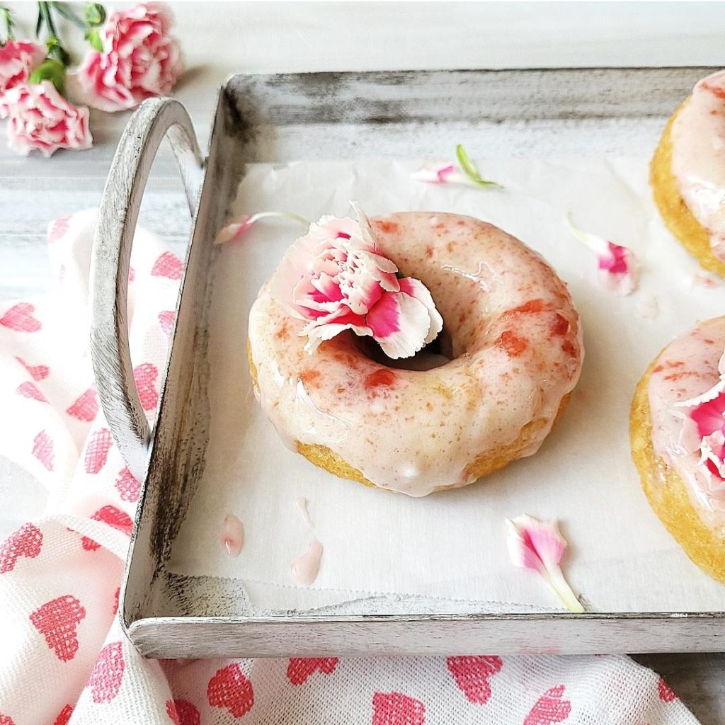 functional image cherry donuts closeup of donut with cherry vanilla glaze and pink carnations on a distressed gray tray with a white linen with pink hearts