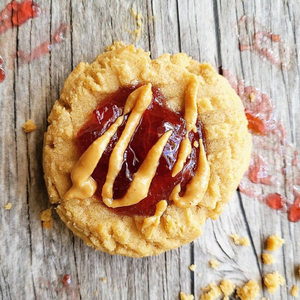 peanut butter and jelly cookies top down close up of one cookie with peanut butter drizzle pbj cookie peanut butter thumbprint cookies