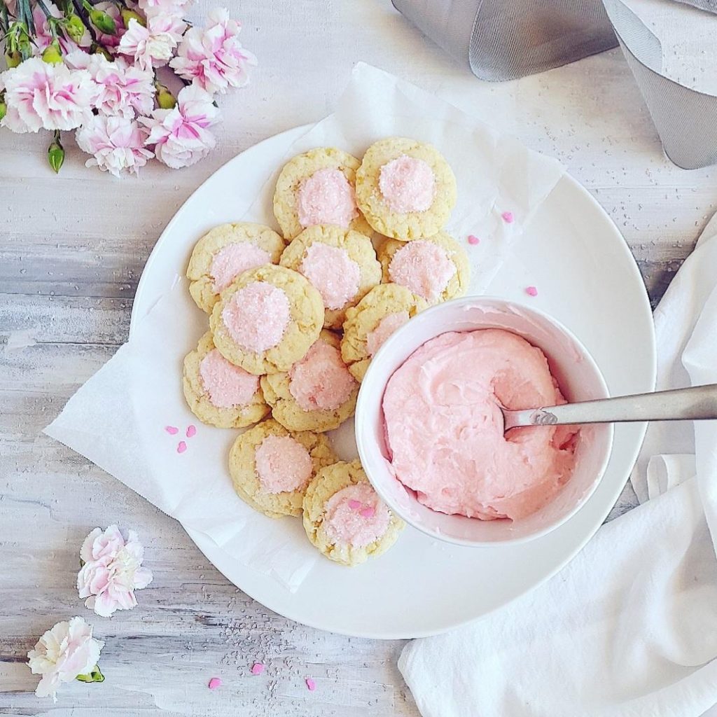functional image thumbprint cookies with icing top down on a white plate with a bowl of pink icing