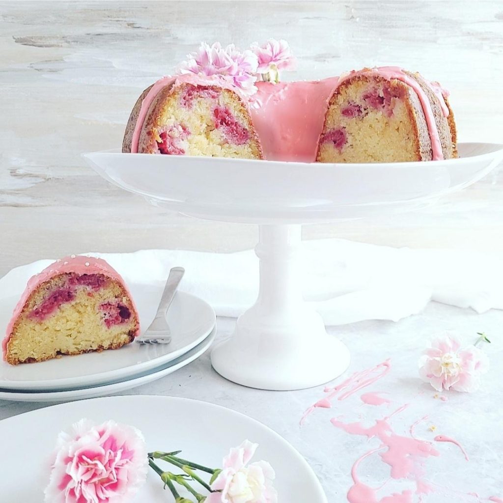 functional image white chocolate raspberry bundt cake side view on a white cake stand cake is cut so you can see the moist crumbs and juicy raspberries