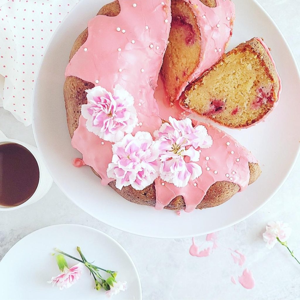 functional image white chocolate raspberry bundt cake top down with two slices cut and askew. garnished with pink glaze pink carnations and white sprinkles