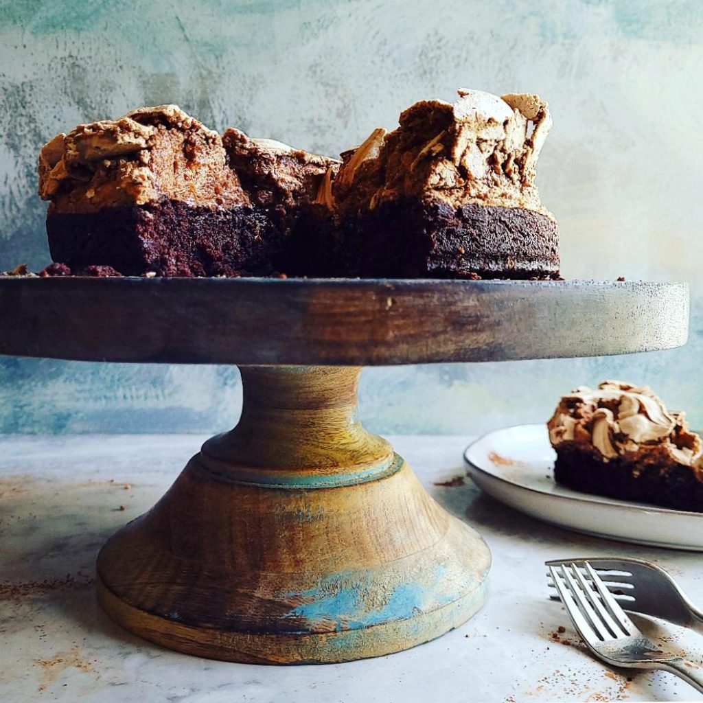 functional image brownie cake cut close up on a wooden cake stand slice of cake in back two forks in front. backdrop is blue