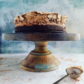 functional image brownie cake with chocolate meringue on a cake stand uncut with blue background