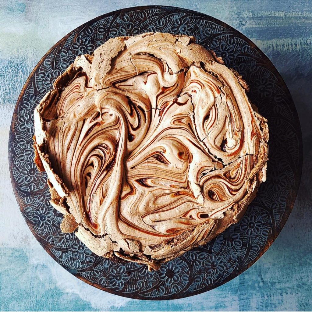 functional image brownie cake with chocolate meringue top down uncut on a brown and blue cake stand on a blue background