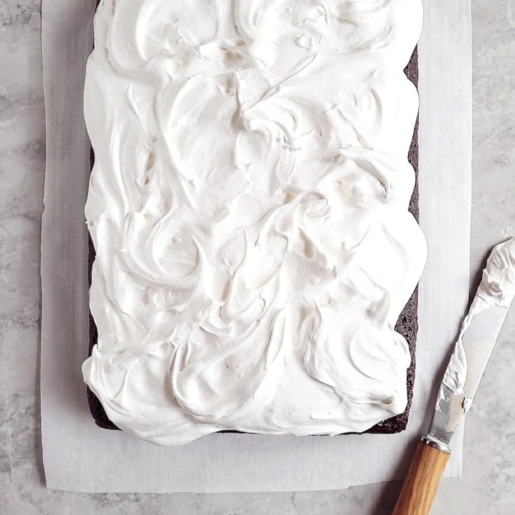 functional image chocolate cake with homemade marshmallow frosting top down uncut with a marshmallow covered spatula with a wooden handle