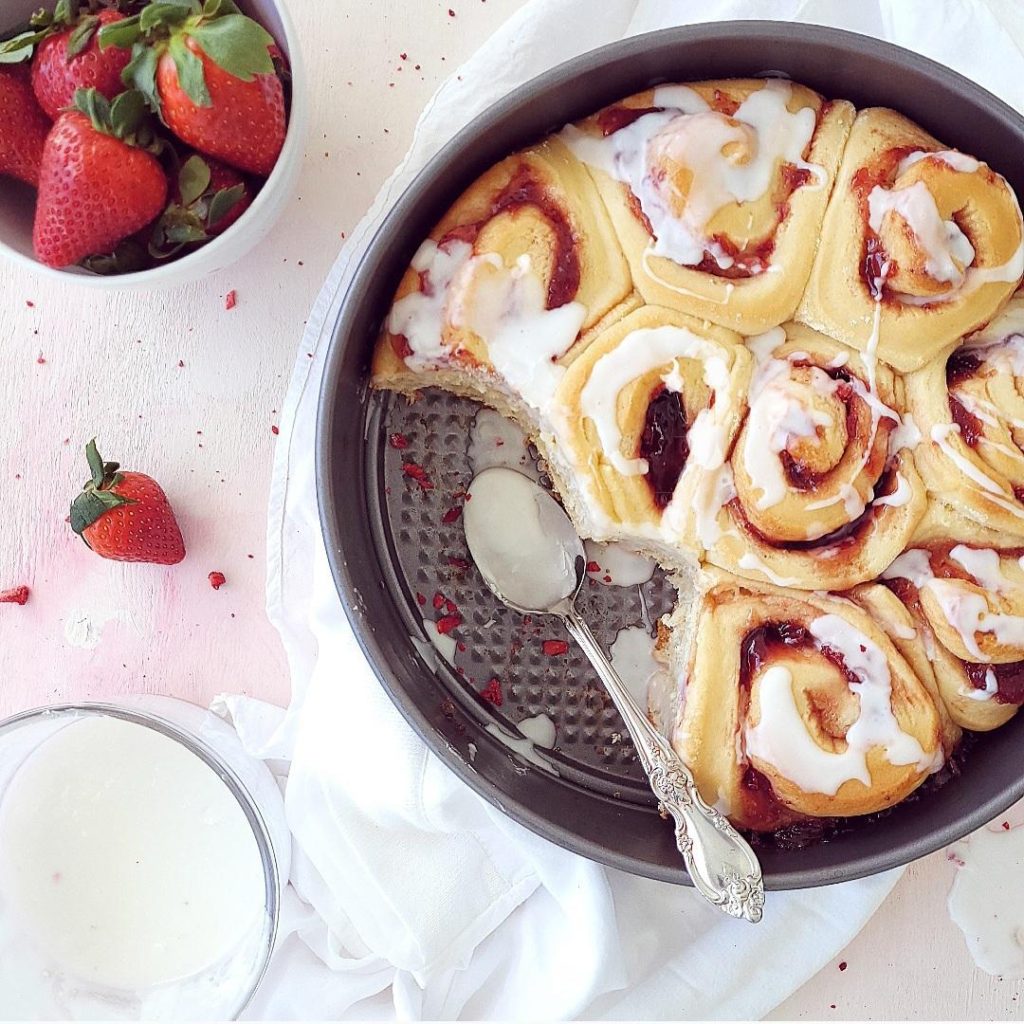 functional image strawberry cinnamon rolls top down in a springform pan topped with vanilla glaze two rolls have been removed from the pan