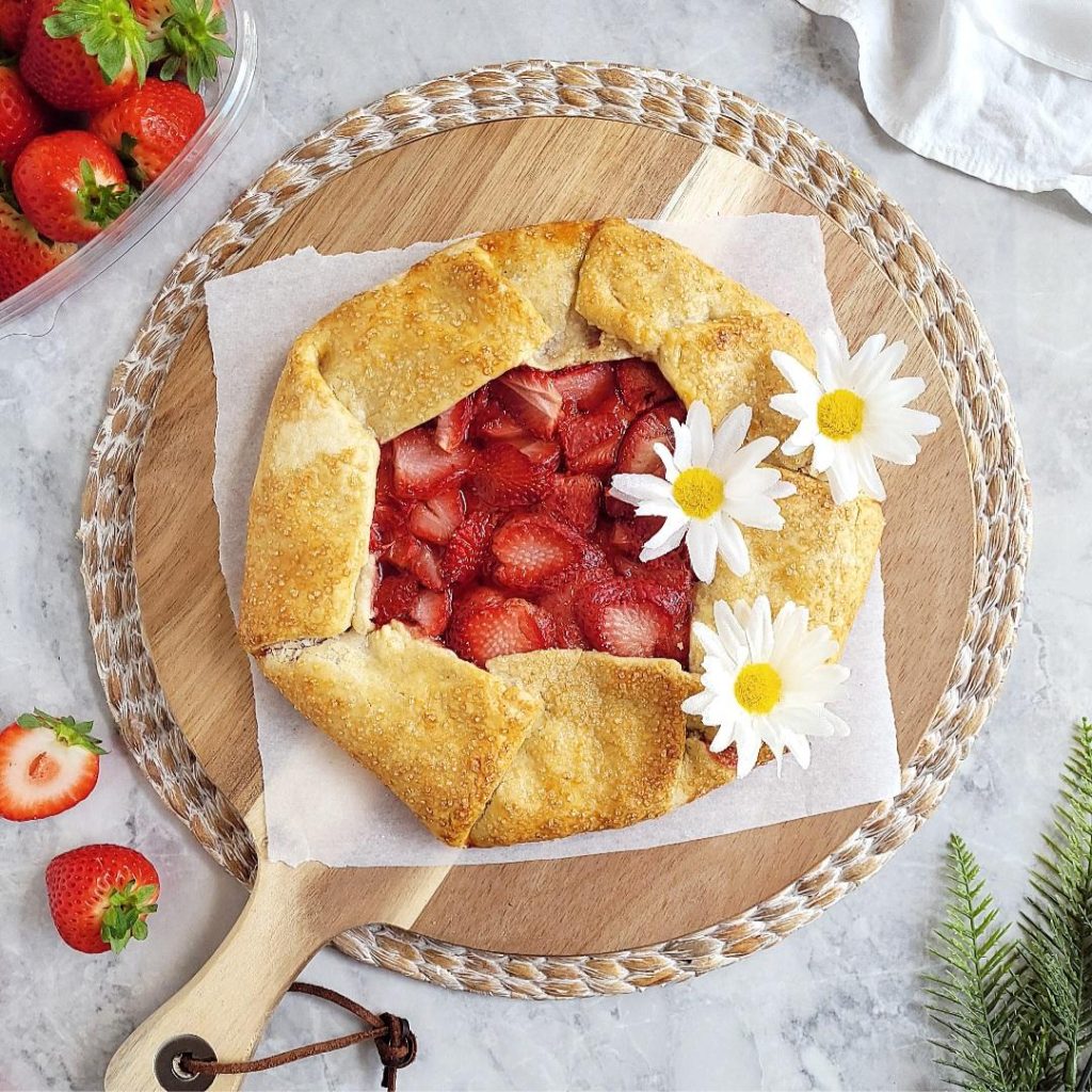 functional image strawberry galette top down with three daisies on crust styled with fresh strawberries on a round wooden cutting board
