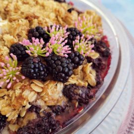 functional image blackberry crisp in a glass baking dish with fresh blackberries and tiny pink flowers zoomed in close and cropped
