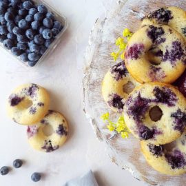functional image blueberry donuts top down on a distressed wooden plate with a carton of blueberries and yellow flowers