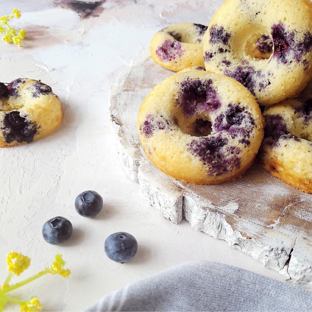 functional image baked blueberry donuts piled on a distressed wooden plate styled with fresh blueberries and yellow flowers