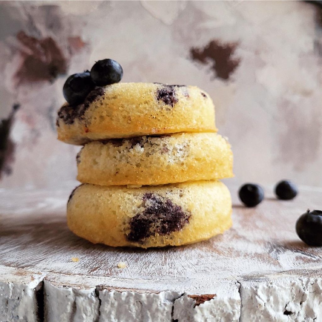 functional image blueberry donuts stacked three high on a whitewashed piece of wood abstract art background with fresh blueberries on top and off to the side 