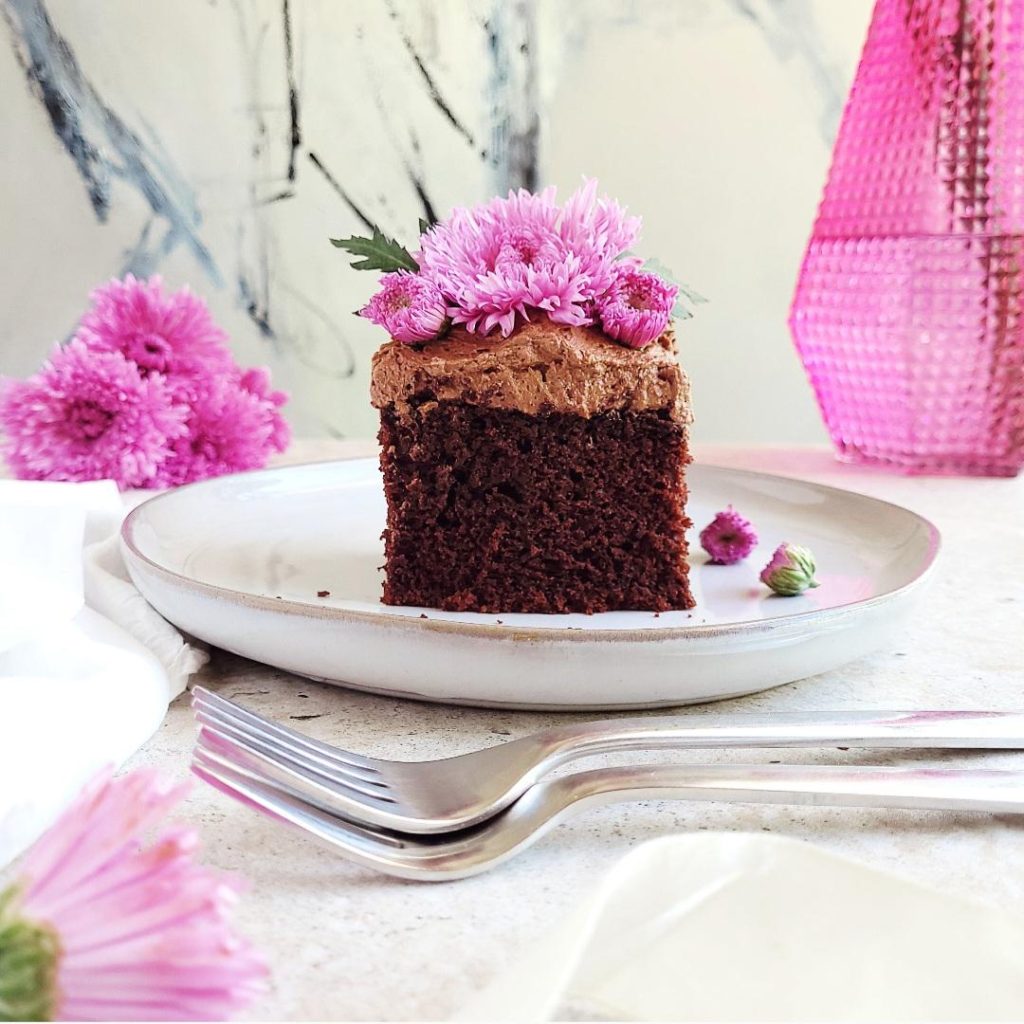 functional image nutella sheet cake with nutella frosting one slice cut on a plate styled with purple flowers and a purple vase